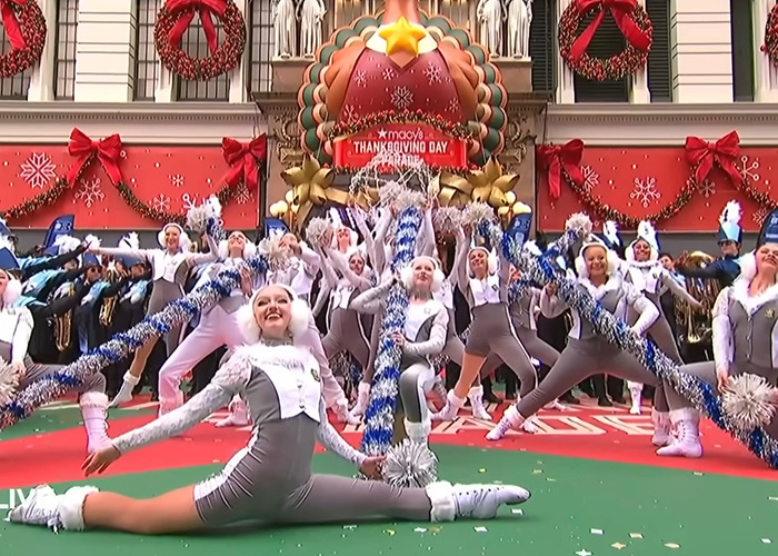 Cheerleaders performing at Macy’s Thanksgiving Day Parade with festive decorations and holiday crowd in background. Cheerleaders performing at Macy’s Thanksgiving Day Parade with festive decorations and holiday crowd in background.