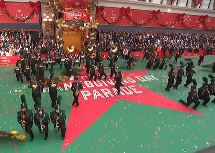 Marching band performing at Thanksgiving parade with festive decorations and large crowd watching the event live Marching band performing at Thanksgiving parade with festive decorations and large crowd watching the event live