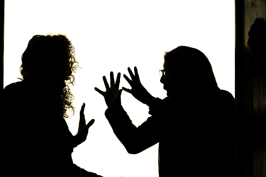 Silhouettes of two women arguing intensely indoors, illustrating a conflict about dangerous parenting and toddler behavior.