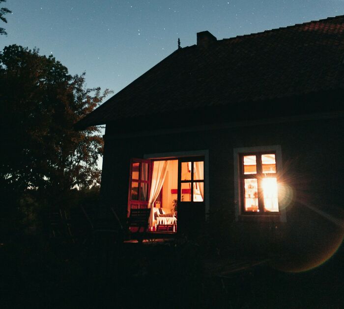 Dark house at night with warm light shining through windows, captured by surveillance cameras for eerie atmosphere.