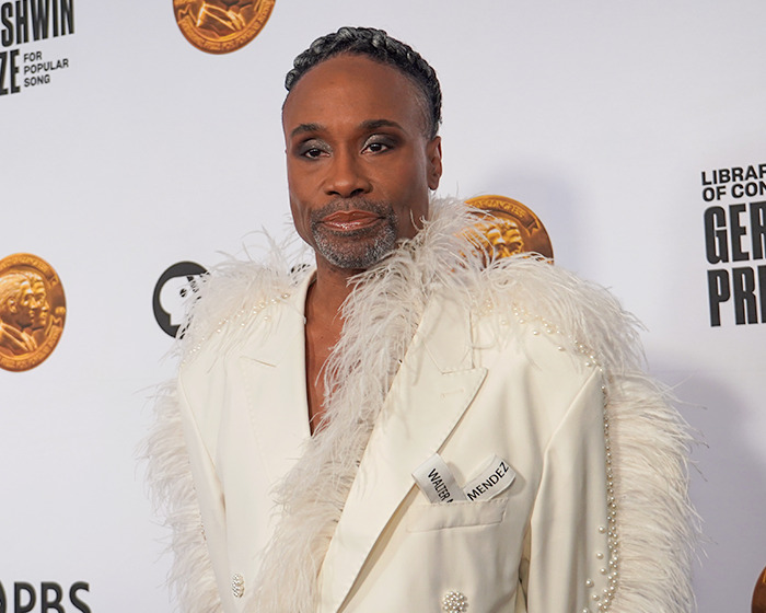 Actor at an event showcasing iconic Hunger Games characters and actors in the new film, wearing a white feathered jacket.