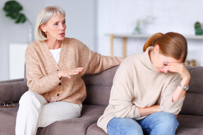 Two women having an emotional conversation on a couch, illustrating a bride told to buy a cheaper bridal gown.