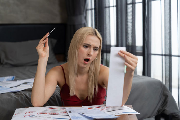 Woman shocked by expensive bridal gown price, surrounded by bills, reacting to wedding dress cost and budget concerns.