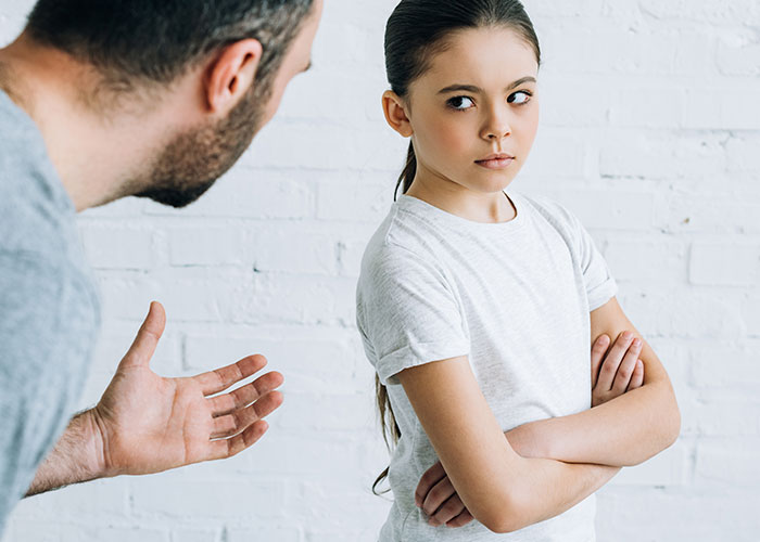 Man talking to teenage girl with rude attitude, arms crossed and avoiding eye contact in a tense family moment.
