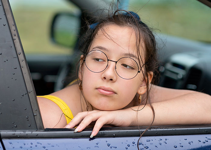 Teen with rude attitude leaning out of car window, showing signs of family tension and frustration over five years.