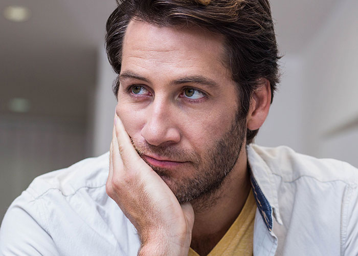 Man with a thoughtful expression resting his face on his hand, reflecting on teen&rsquo;s rude attitude and family struggles.
