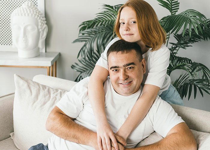 Man and teen girl sitting on couch at home, showing family relationship and teenage attitude.