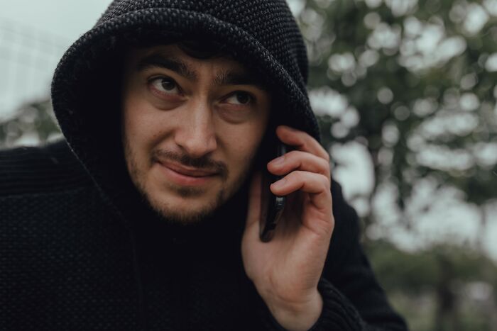 Man in black hoodie speaking on phone outdoors, symbolizing people who fell for scams and its impact on them.