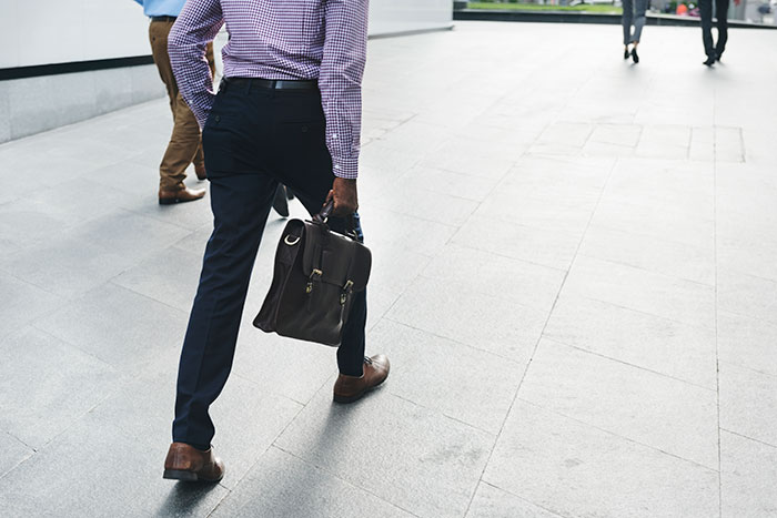 Employee walking away from office building holding briefcase, illustrating manager letting employee take time off.