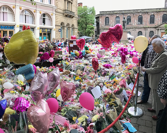 Crowd gathered around a memorial filled with flowers and balloons, reflecting the impact of Ariana Grande's last hurrah announcement.