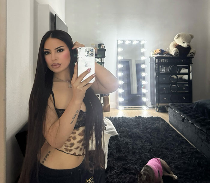 Young woman with long dark hair taking a mirror selfie in a bedroom with a dog lying on the floor nearby. Young woman with long dark hair taking a mirror selfie in a bedroom with a dog lying on the floor nearby.