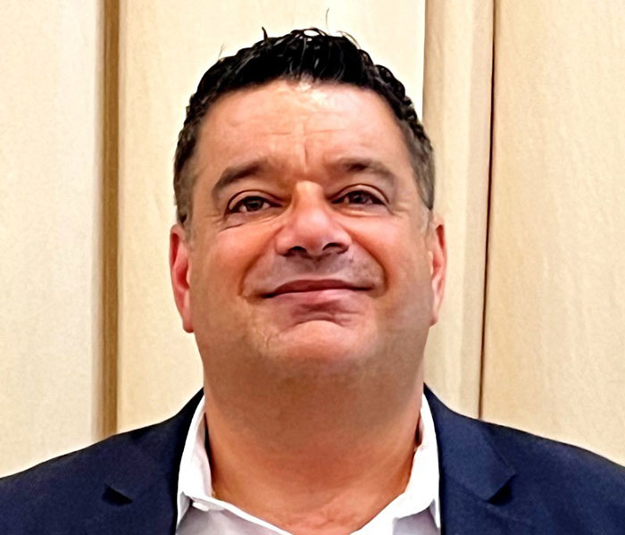 Middle-aged man in a dark suit smiling against a beige background related to Campbell's executive leaked audio on soup ingredients.
