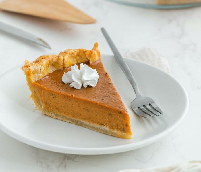 Slice of pumpkin pie with whipped cream on a white plate, representing Thanksgiving food and festive arguments online.