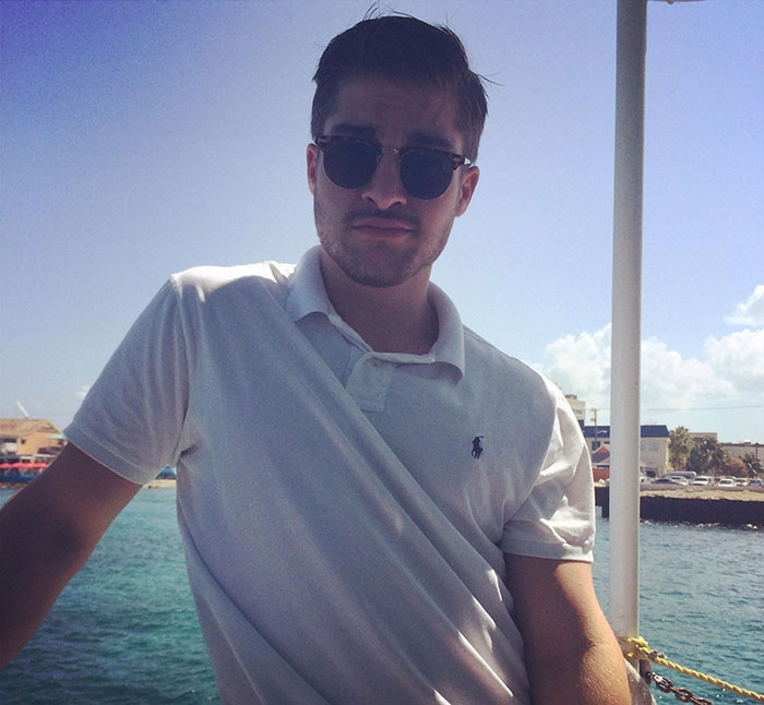 Young man wearing sunglasses and a white polo shirt posing outdoors by the water inspired by the next Brad Pitt viral sensation.