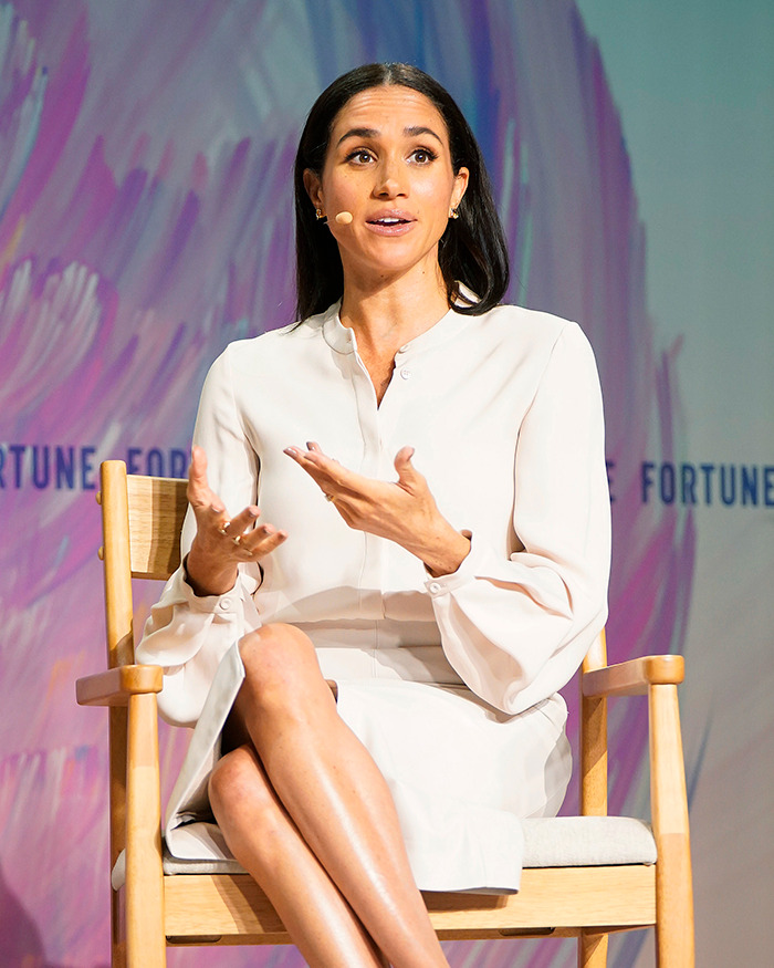 Meghan Markle speaking at an event wearing a white dress, addressing the audience with expressive hand gestures. Meghan Markle speaking at an event wearing a white dress, addressing the audience with expressive hand gestures.