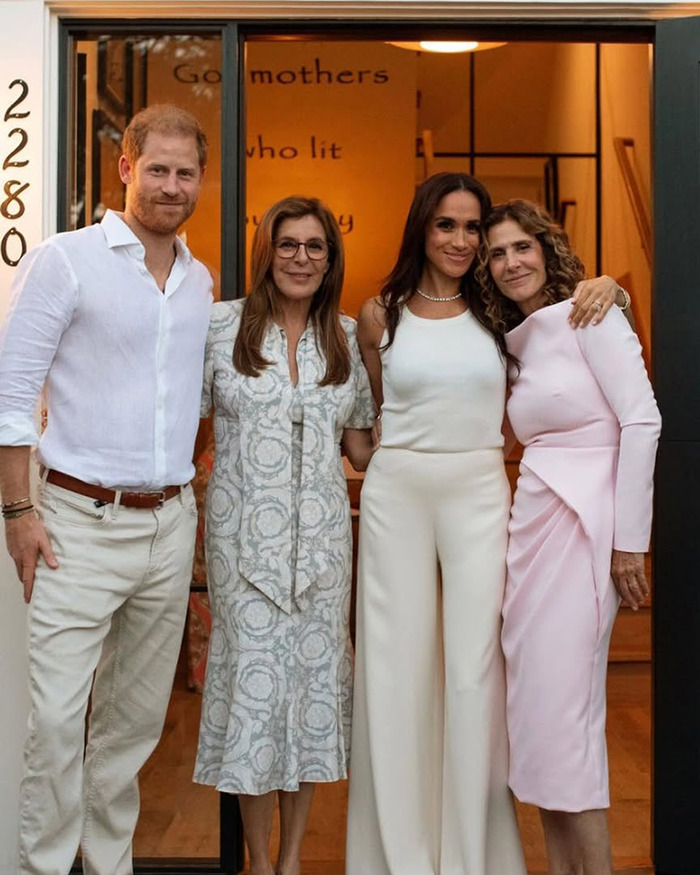 Meghan Markle standing with three people in casual attire inside a warmly lit room during a social event. Meghan Markle standing with three people in casual attire inside a warmly lit room during a social event.