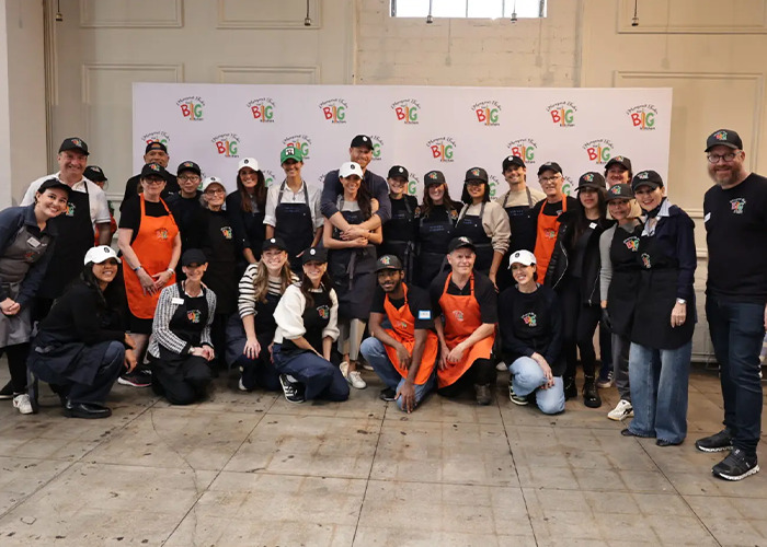 Group of volunteers wearing aprons and caps posing indoors at a charity event related to Meghan Markle royal gesture controversy. Group of volunteers wearing aprons and caps posing indoors at a charity event related to Meghan Markle royal gesture controversy.