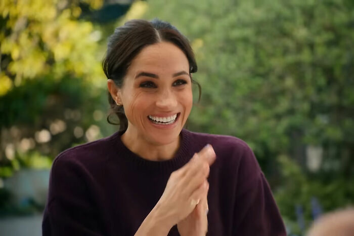 Meghan Markle smiling and clapping during a home celebration with Prince Harry, seen as staged by many viewers.