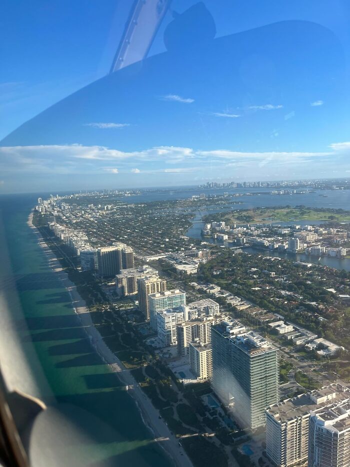Aerial view of Miami coastline with high-rise buildings, beaches, and cityscape under a clear blue sky.