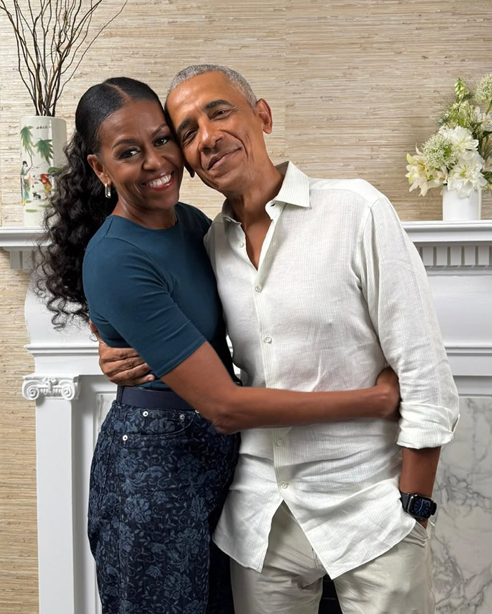 Michelle Obama smiling with ultra-long hair in a casual outfit, embracing Barack Obama indoors by a fireplace. Michelle Obama smiling with ultra-long hair in a casual outfit, embracing Barack Obama indoors by a fireplace.