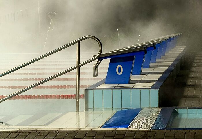 Empty swimming pool lanes with starting blocks in foggy or steamy early morning setting workers share unprofessional things done