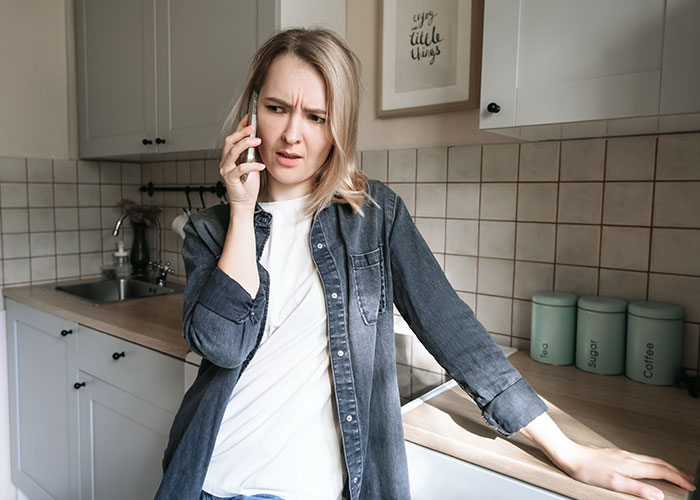 Woman in kitchen talking on phone, looking concerned while expecting Thanksgiving dinner after a 12-hour shift. Woman in kitchen talking on phone, looking concerned while expecting Thanksgiving dinner after a 12-hour shift.