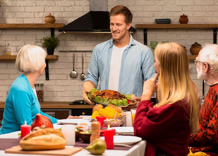 Man bringing Thanksgiving dinner to family sitting at table after a long 12-hour shift, showing mil expects Thanksgiving dinner. Man bringing Thanksgiving dinner to family sitting at table after a long 12-hour shift, showing mil expects Thanksgiving dinner.