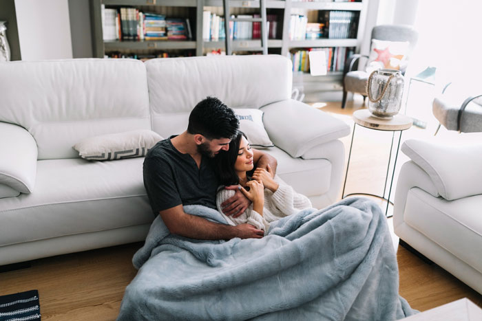 Couple cuddling under a blanket on the floor in a cozy living room, reflecting family holiday tensions with sick DIL excluded. Couple cuddling under a blanket on the floor in a cozy living room, reflecting family holiday tensions with sick DIL excluded.