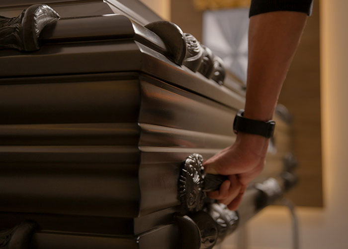 A close-up of a hand gripping a dark ornate coffin handle, illustrating a mildly disturbing fact concept.