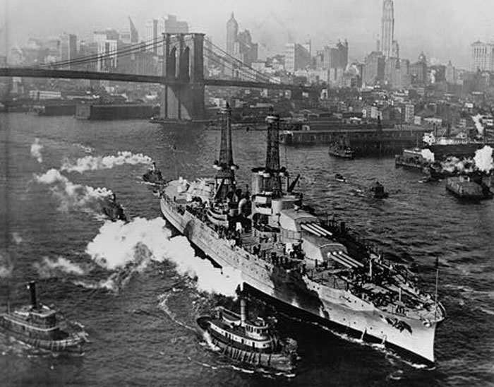 Historic battleship sailing near Brooklyn Bridge with tugboats in New York Harbor, illustrating mildly disturbing fact context.