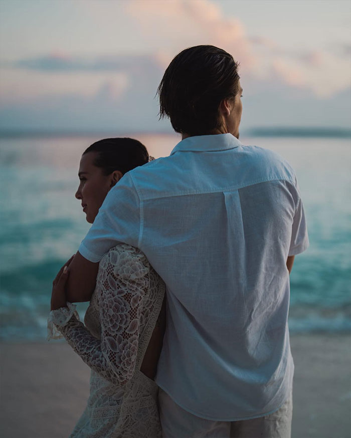 Two people embracing by the ocean at sunset, representing Millie Bobby Brown breaking silence about adopting a baby. Two people embracing by the ocean at sunset, representing Millie Bobby Brown breaking silence about adopting a baby.