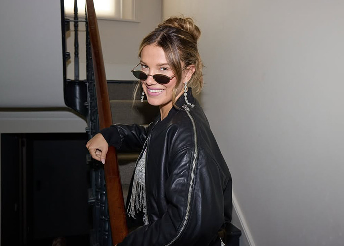 Young woman wearing sunglasses and a leather jacket smiling on stairs, related to Millie Bobby Brown Stranger Things rumors.