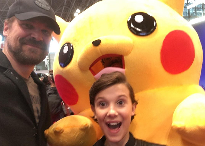 David Harbour and Millie Bobby Brown smiling with a large Pikachu mascot at a public event, Stranger Things cast photo.