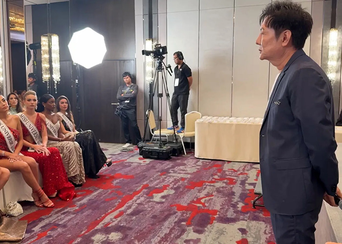 Miss Universe contestants seated in gowns facing a man in a suit during a tense moment at the event.