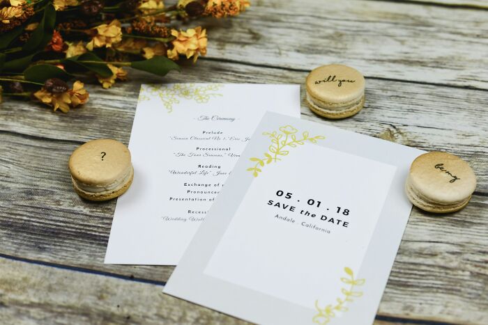 Wedding invitations and macarons with calligraphy on a rustic wooden table, highlighting wedding event planning.