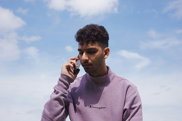 Young man in a purple sweatshirt talking on phone outdoors, reflecting on toxic girlfriend and relationship ultimatum situation