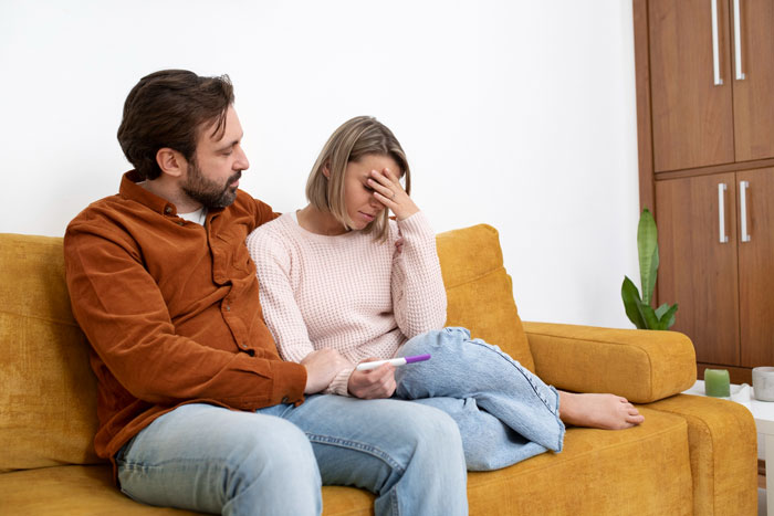 Couple sitting on a couch with the woman upset holding a pregnancy test, capturing a moment of mom affair concern and dad support.