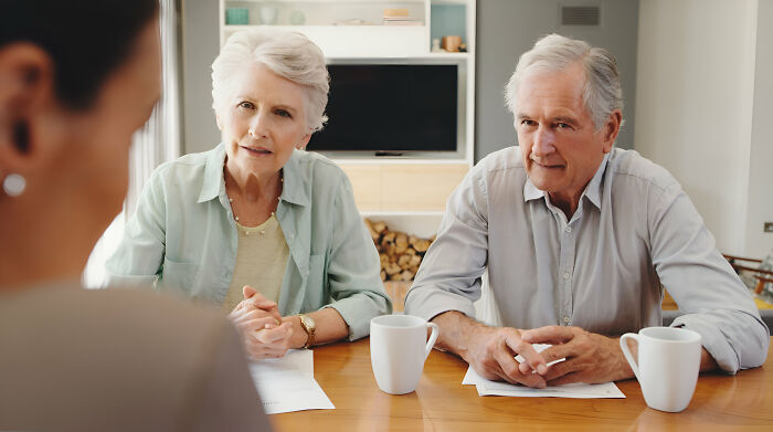 Older father-in-law and mother-in-law discussing paperwork with daughter-in-law, showing tension in a home setting.