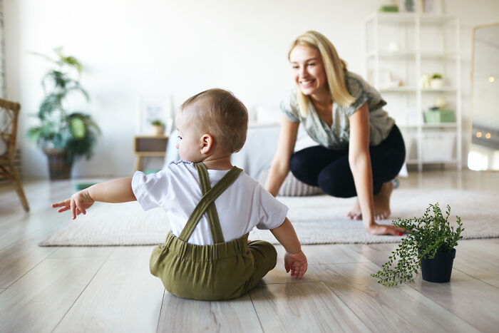 Baby sitting on the floor with mother smiling nearby in bright home, relating to father-in-law treats DIL like dirt situation.