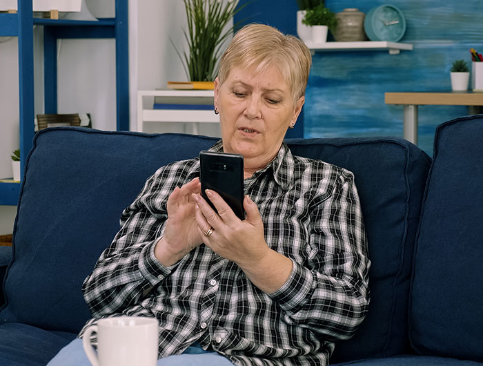 Older woman on couch looking at phone with concern, illustrating man cutting ties with mother after revealing true colors.