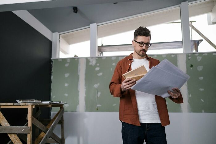 Man in glasses and casual clothes reviewing building plans, illustrating inventive ways workers got away with breaking rules.