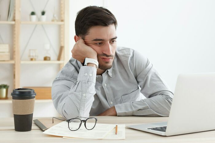 Man in gray shirt looking bored at laptop, showcasing hilarious and inventive ways workers got away with breaking rules.