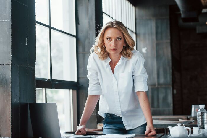 Woman in a white shirt leaning on a desk in an office, illustrating inventive ways workers got away with breaking rules.