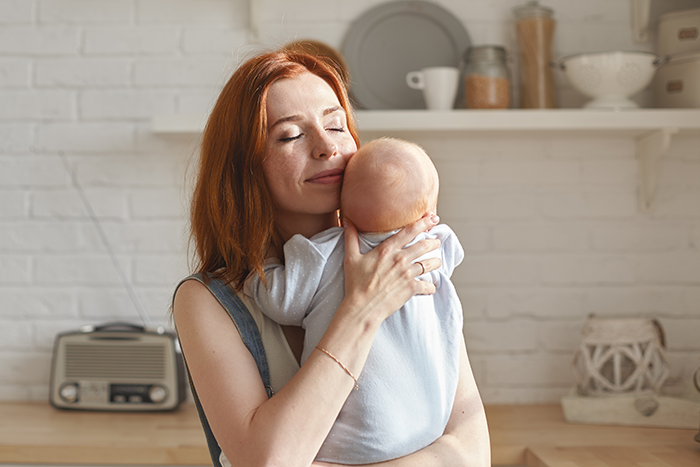 Woman gently holding a newborn baby nephew, reflecting sibling refuse newborn nephew care concerns in a bright kitchen.