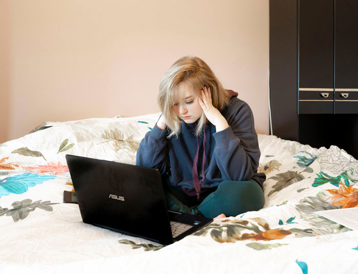 Young woman looking stressed while using a laptop on bed, relating to therapy sessions and trust issues with mom.
