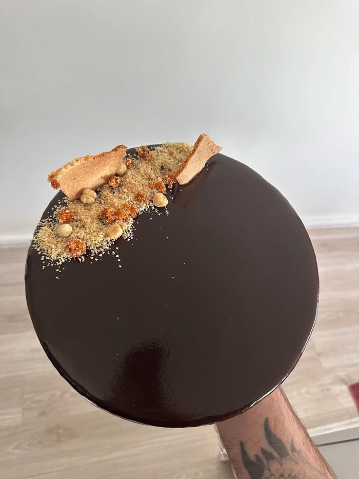 Glossy chocolate-covered baked good topped with crumbs, nuts, and caramel pieces, showcasing gorgeous baked goods artistry.