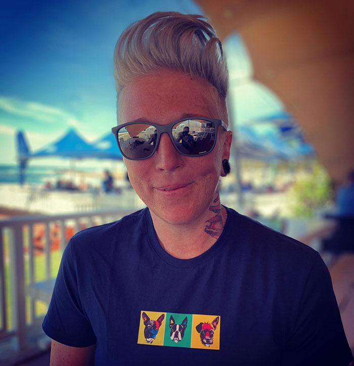 Celebrity chef wearing sunglasses, with short hairstyle, smiling outdoors at a sunny location with tents in background.