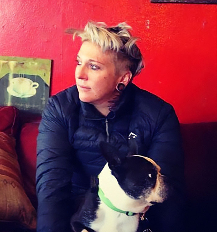 Celebrity chef sitting on a couch with a dog, wearing a black jacket, in a room with red walls.
