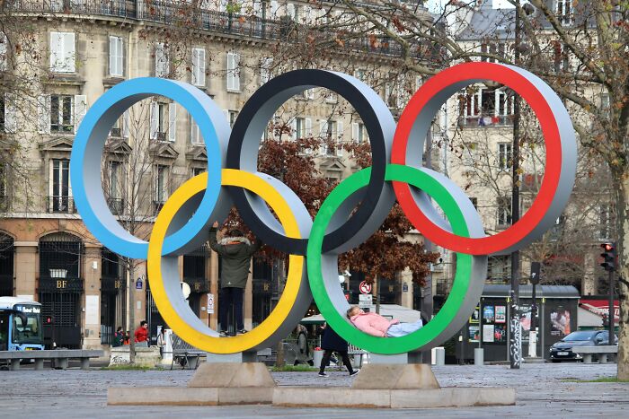 Olympic rings sculpture in a city park with people interacting, illustrating insider experiences of nepo babies.