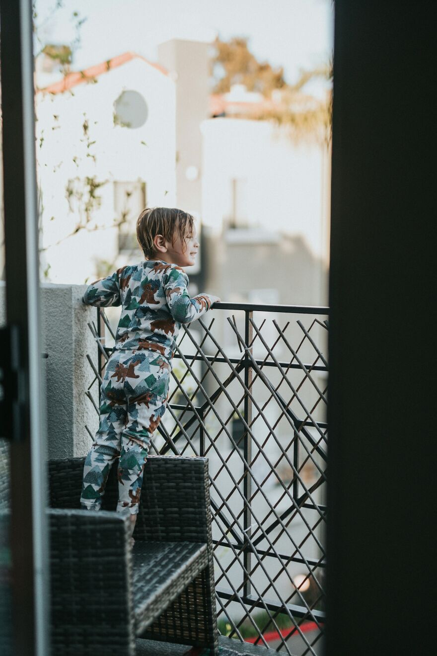 Toddler standing on chair looking over balcony rail in pajamas, related to dangerous parenting and cats energy drinks concerns.